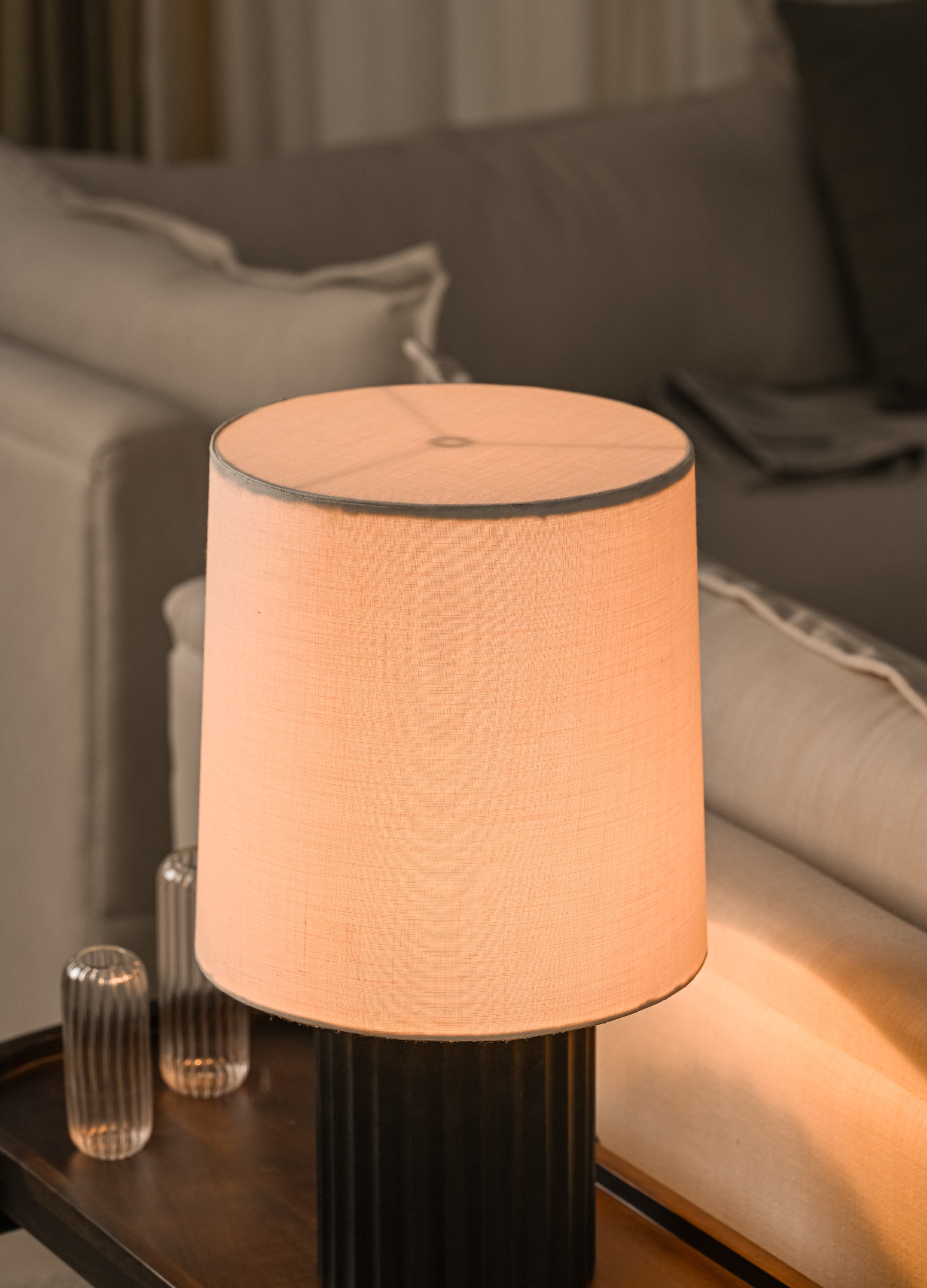 Black Table lamp with a beige shade on a wooden side table in a living room setting.