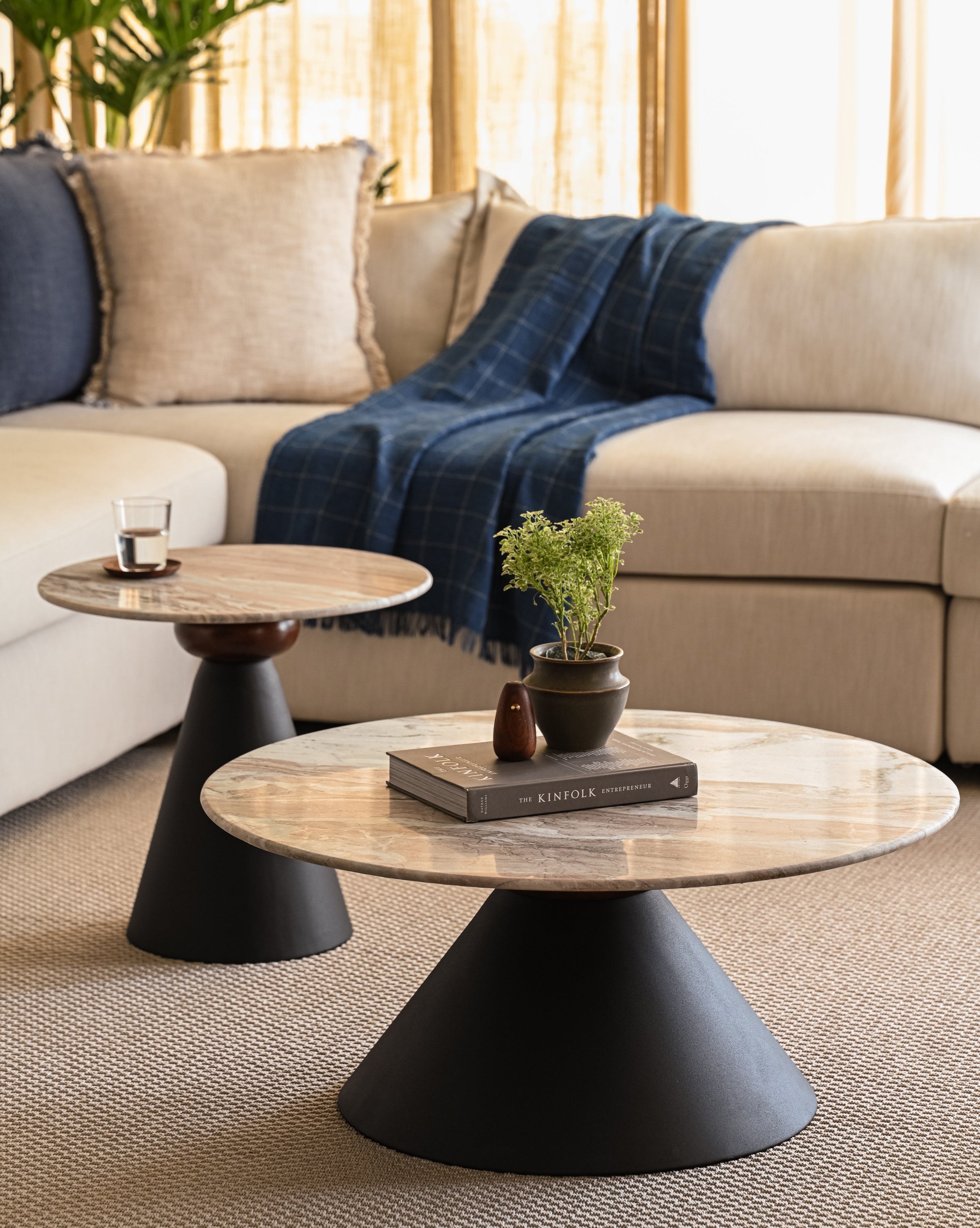 Round marble coffee table and accent table nested with matte black bases styled with books and plants.