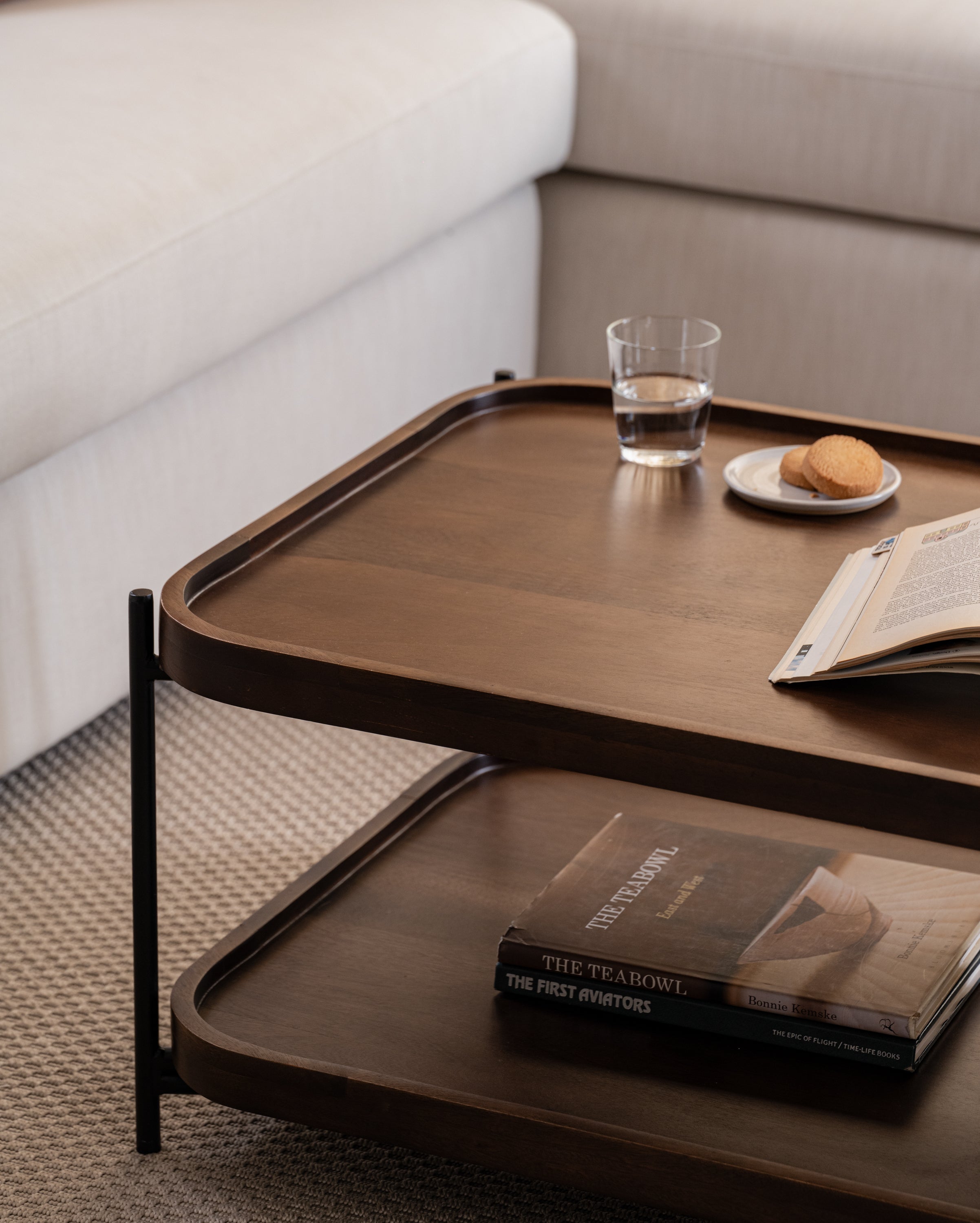 Close up of rectangular coffee table with rich wood finish and matte black frame, styled with books and glassware.