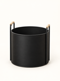 A matte black cylindrical metal planter or basket with two vertical side handles and light natural wood grips, shown on a clean white background.