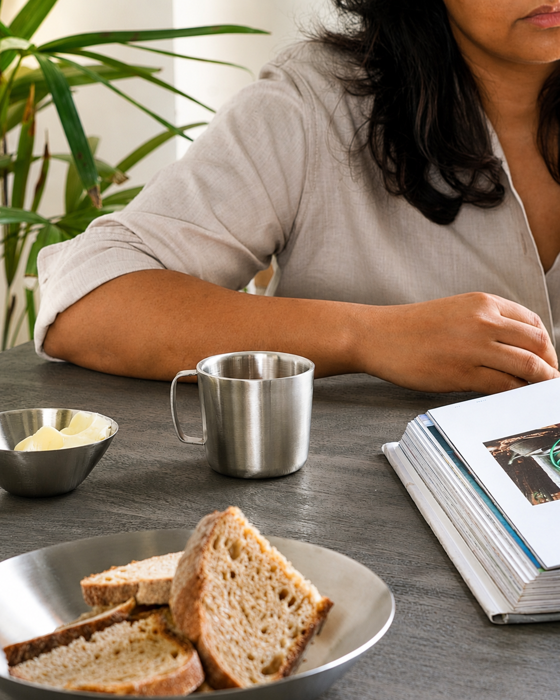 Person sitting at a table with bread, a cup, and a book in a casual setting.