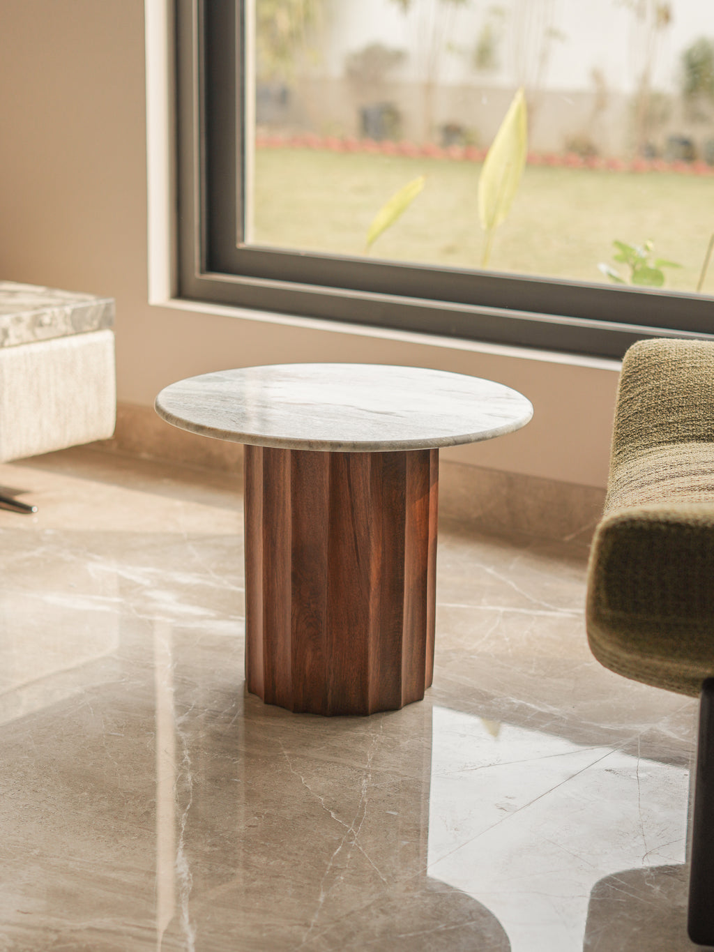 Round marble table with wooden base in a room with a large window.