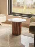 Round marble table with wooden base in a room with a large window.