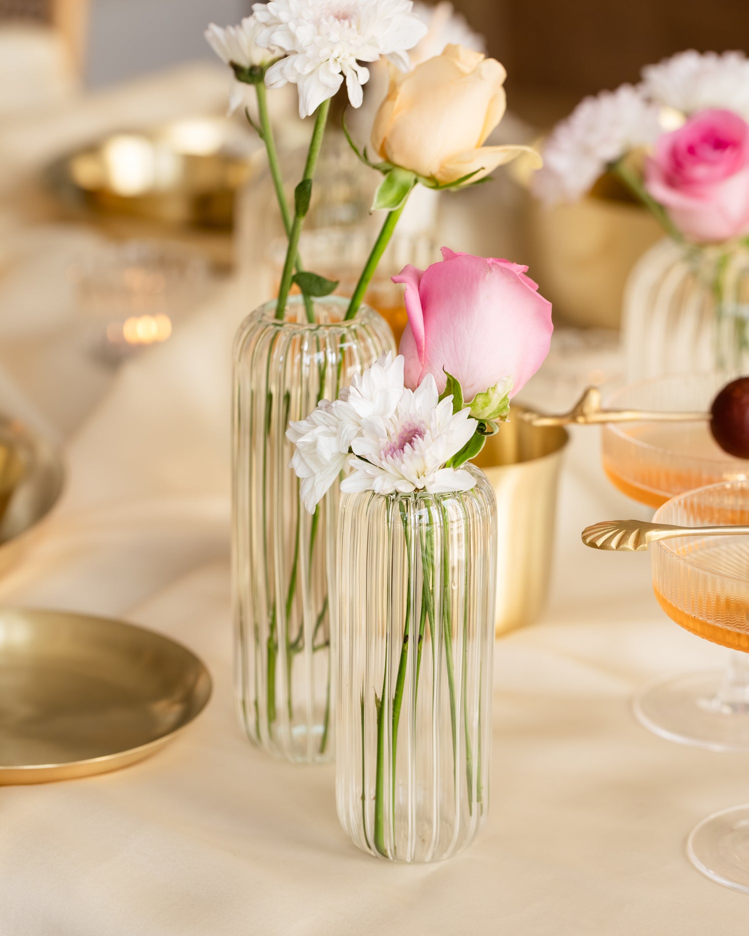 Clear glass flower vase with pink roses, placed on a white tablecloth. 