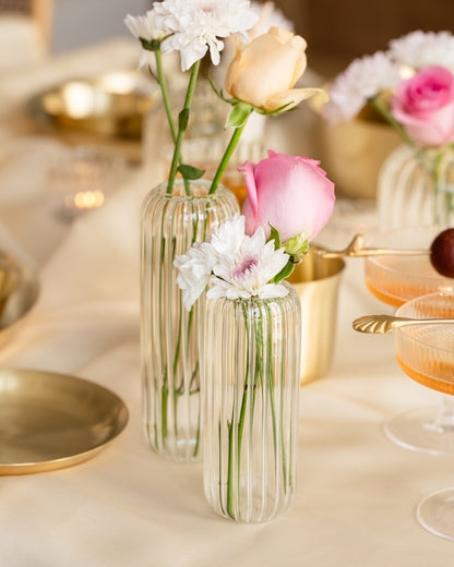 Clear glass flower vase with pink roses, placed on a white tablecloth. 