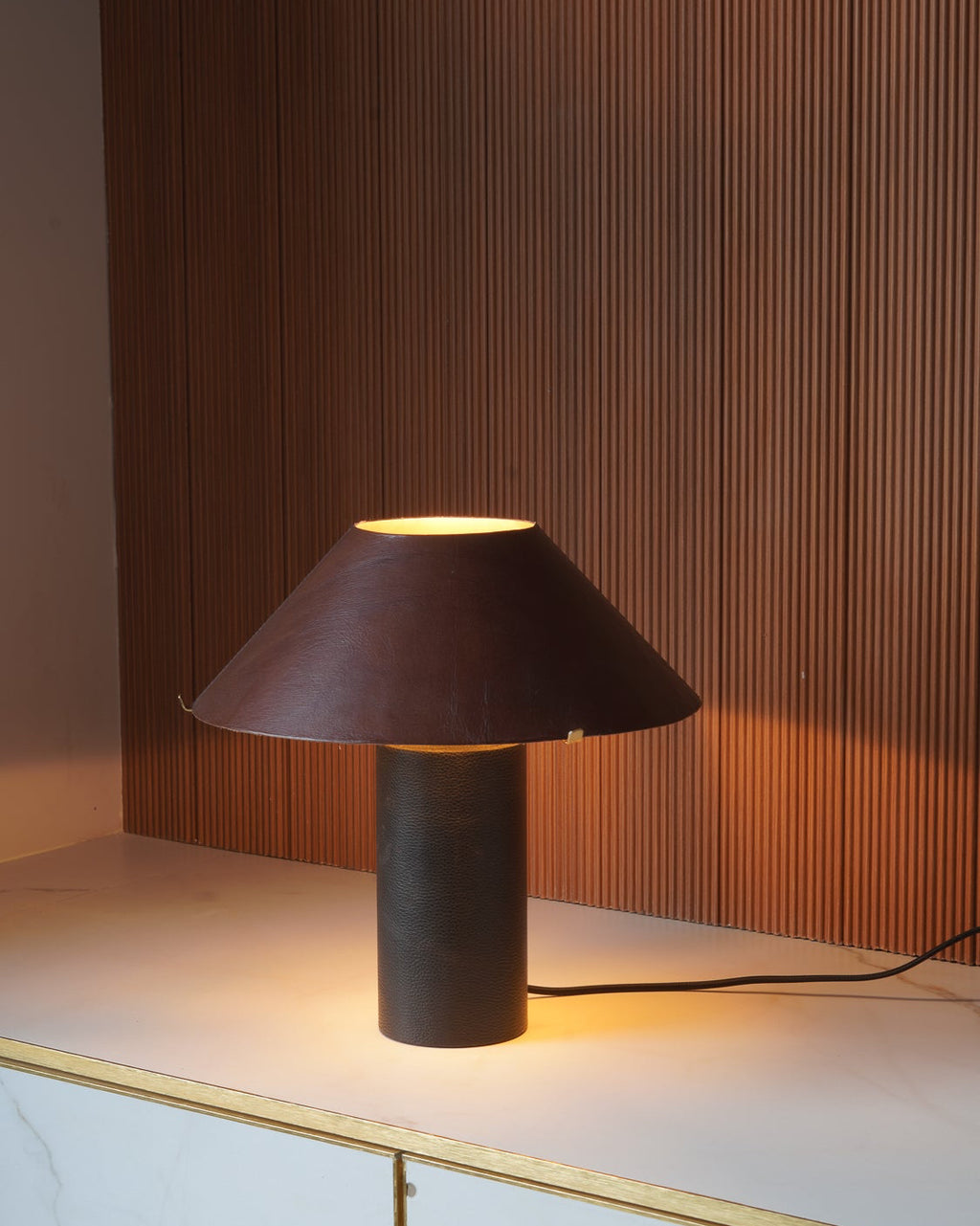 Modern table lamp made with leather with a brown shade on a marble surface with wooden panel background
