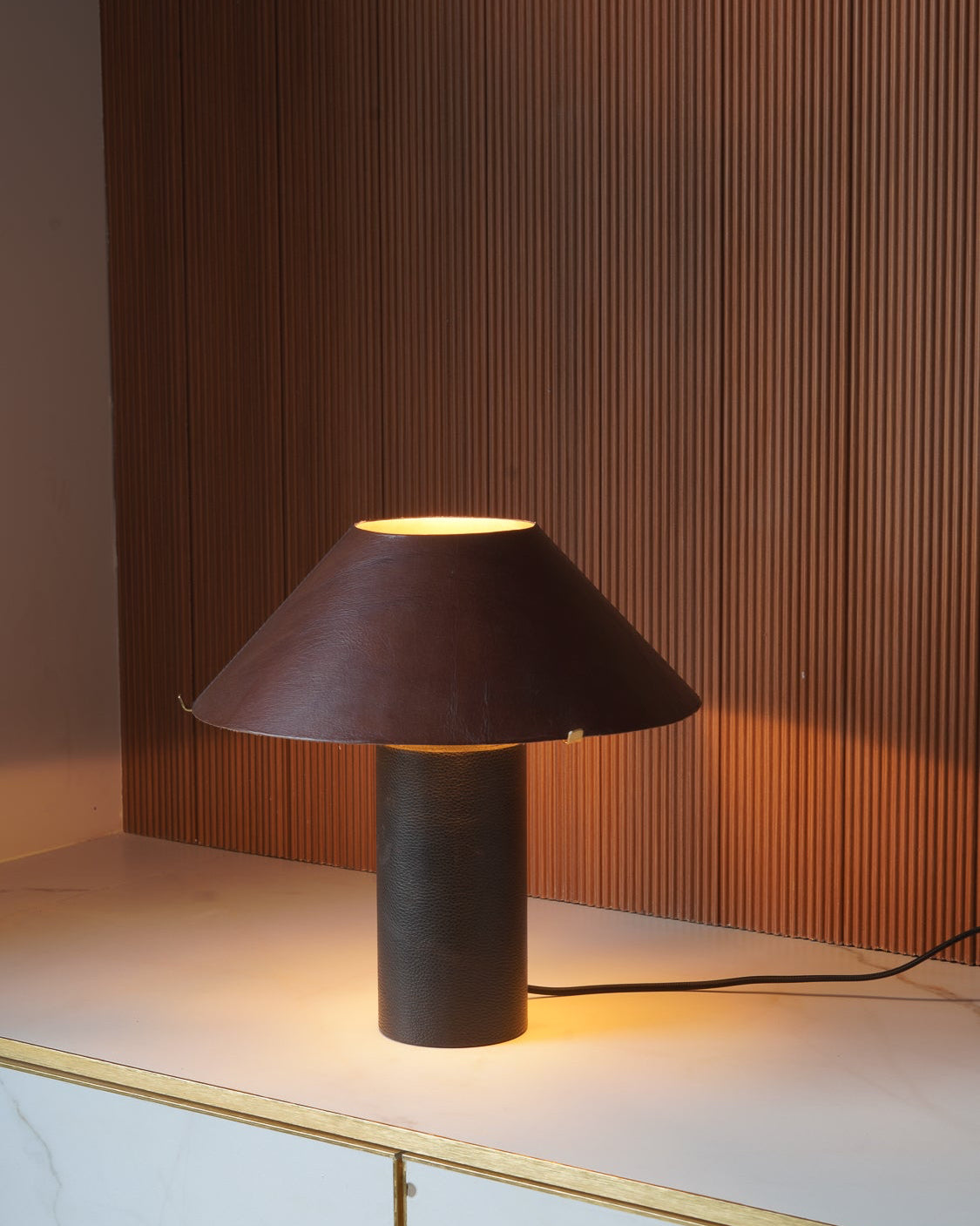 Modern table lamp made with leather with a brown shade on a marble surface with wooden panel background