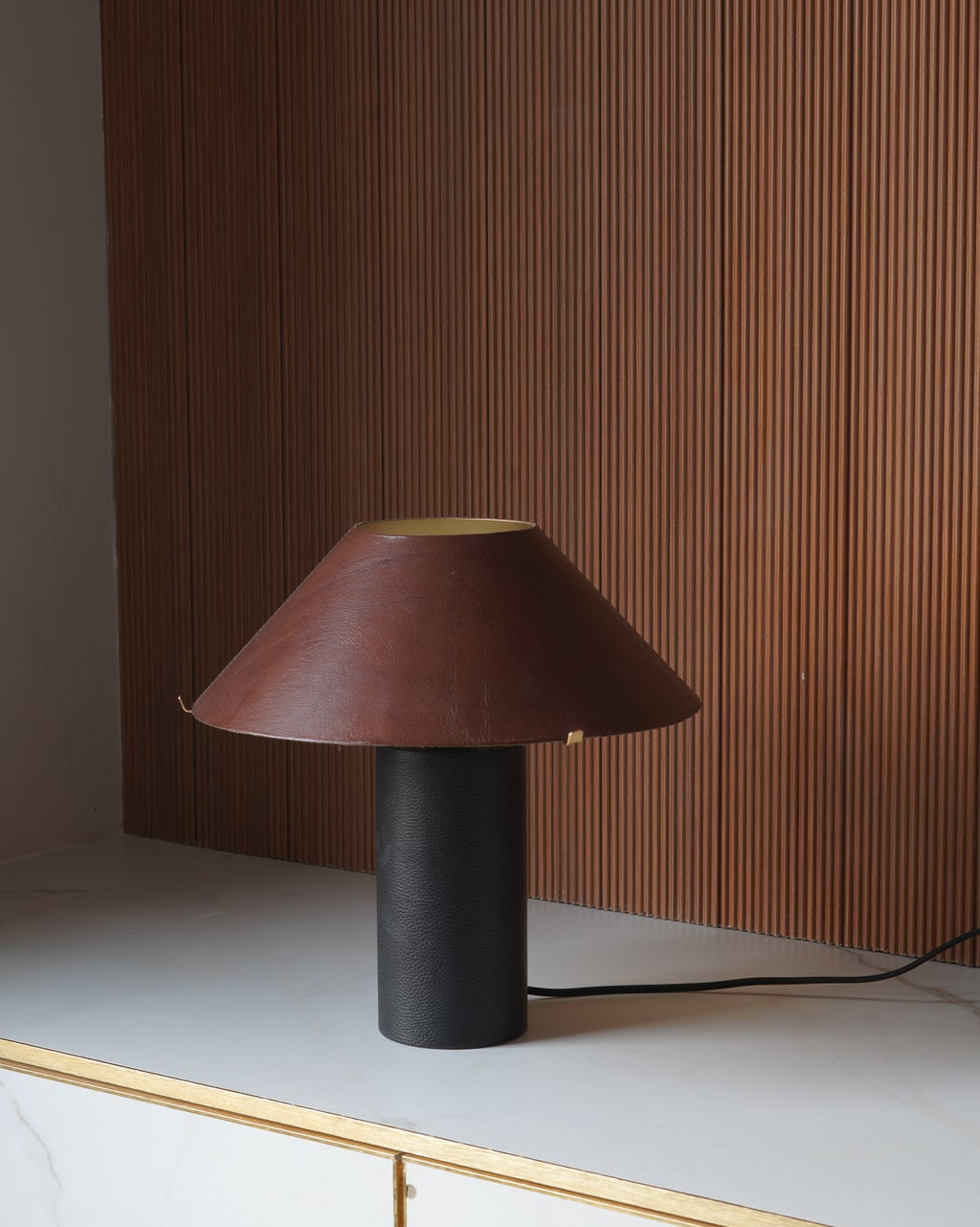Table lamp with a brown shade and black base on a white surface with a wooden panel background