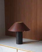 Table lamp with a brown shade and black base on a white surface with a wooden panel background