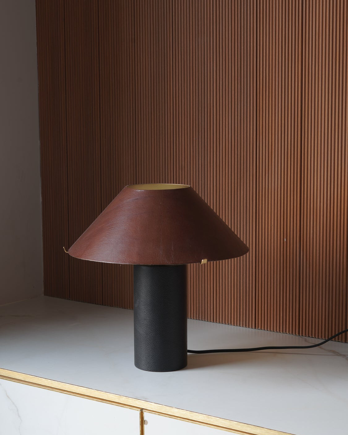 Table lamp with a brown shade and black base on a white surface with a wooden panel background