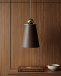Pendant light with brown shade and gold fixture on a wooden wall.