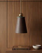 Pendant light with brown shade and gold fixture on a wooden wall.