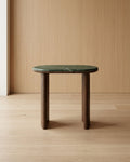 Small table with green marble top and wooden legs against a wooden wall.