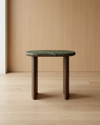 Small table with green marble top and wooden legs against a wooden wall.