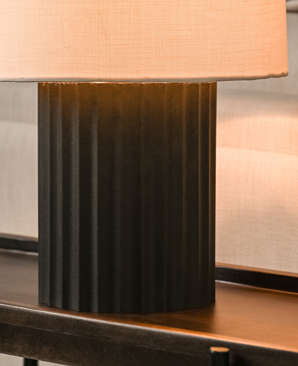 Table lamp with a black base and peach-colored shade on a wooden surface.