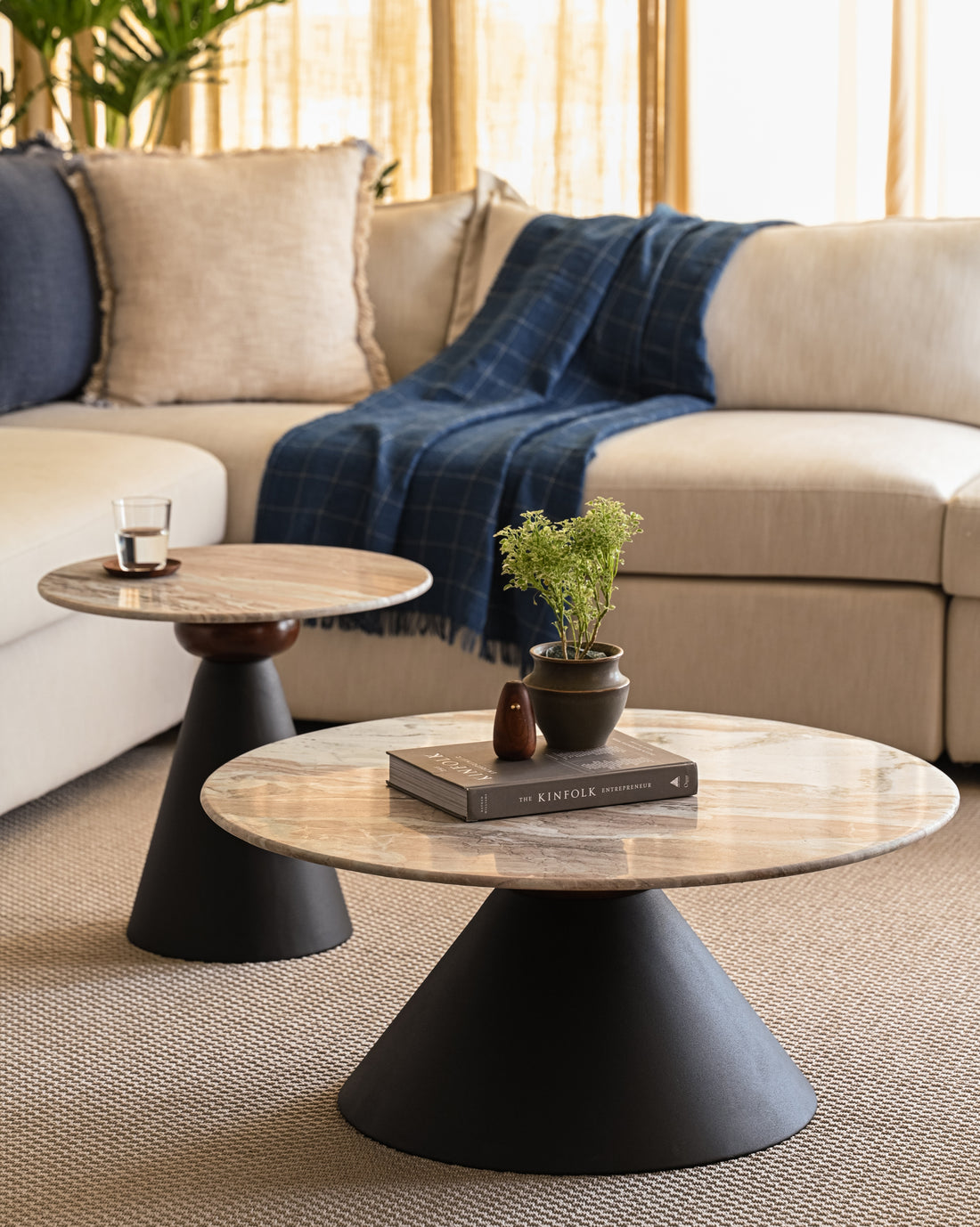 Round marble coffee table and accent table nested with matte black bases styled with books and plants.