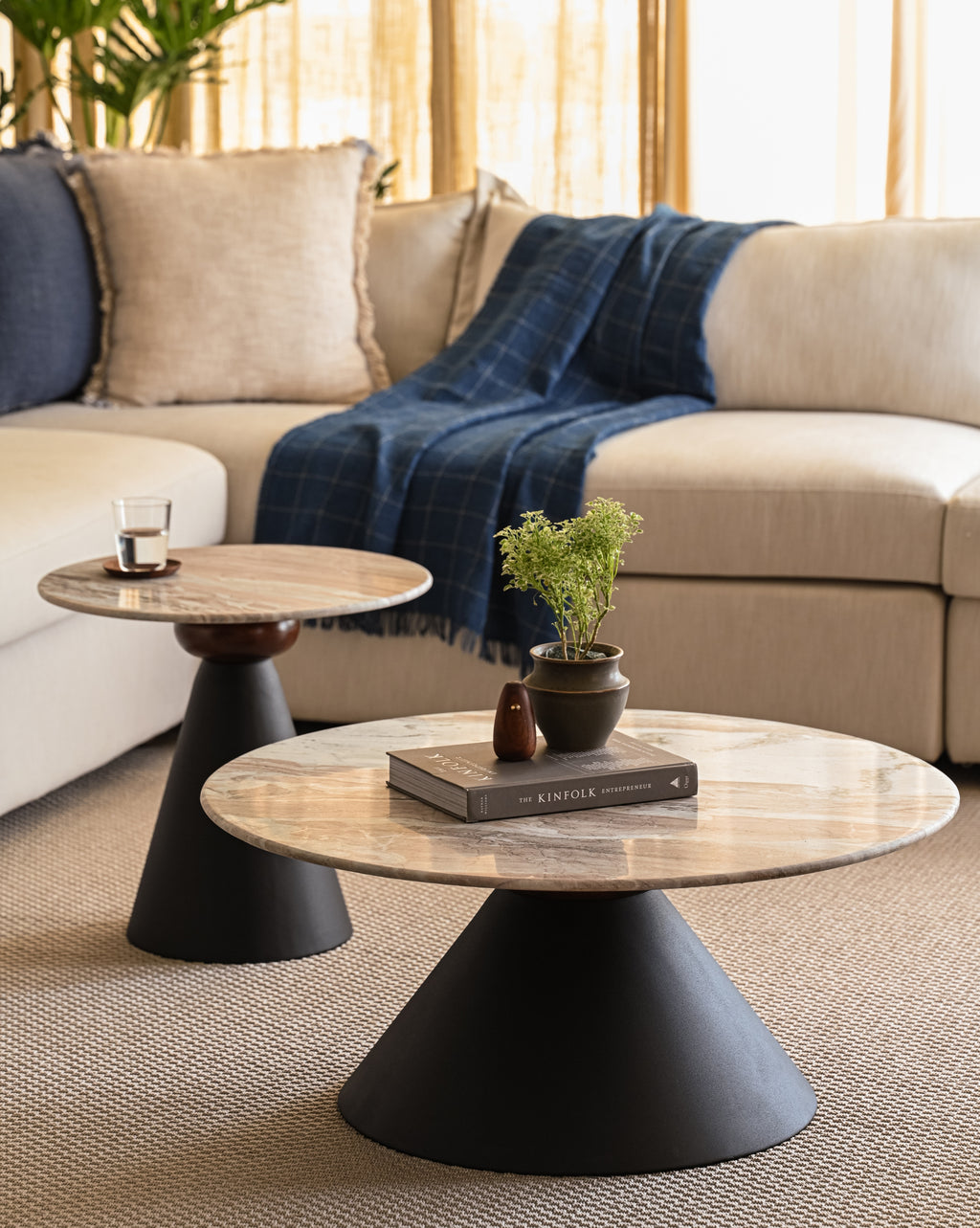 Round marble coffee table and accent table nested with matte black bases styled with books and plants.
