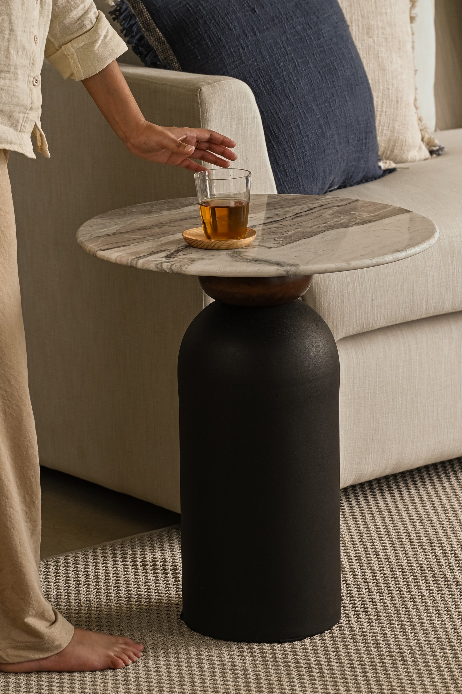 Side table with marble top and cylindrical black stand, next to a couch.