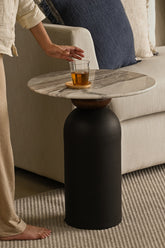 Side table with marble top and cylindrical black stand, next to a couch.