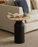 Round marble side table with black pedestal base, placed beside a beige sofa.