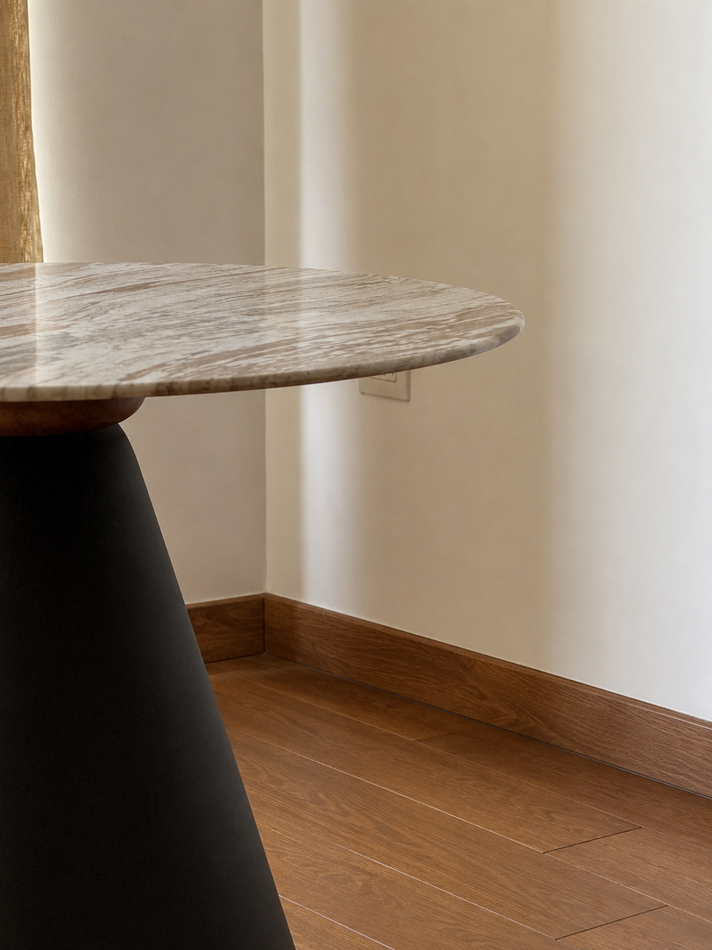 A close-up of a modern round table with a polished gray and white marble top and a dark tapered base, set in a room with beige walls and wood flooring.