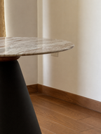 A close-up of a modern round table with a polished gray and white marble top and a dark tapered base, set in a room with beige walls and wood flooring.