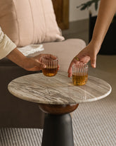 Close-up of modern marble drinks table with black base and glasses being picked up.