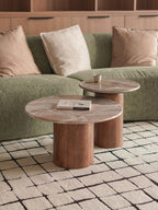 Two wooden coffee nesting tables in front of a green sofa with beige cushions on a tiled floor.