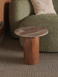 Wood and marble side table in front of a green sofa with a neutral pillow.