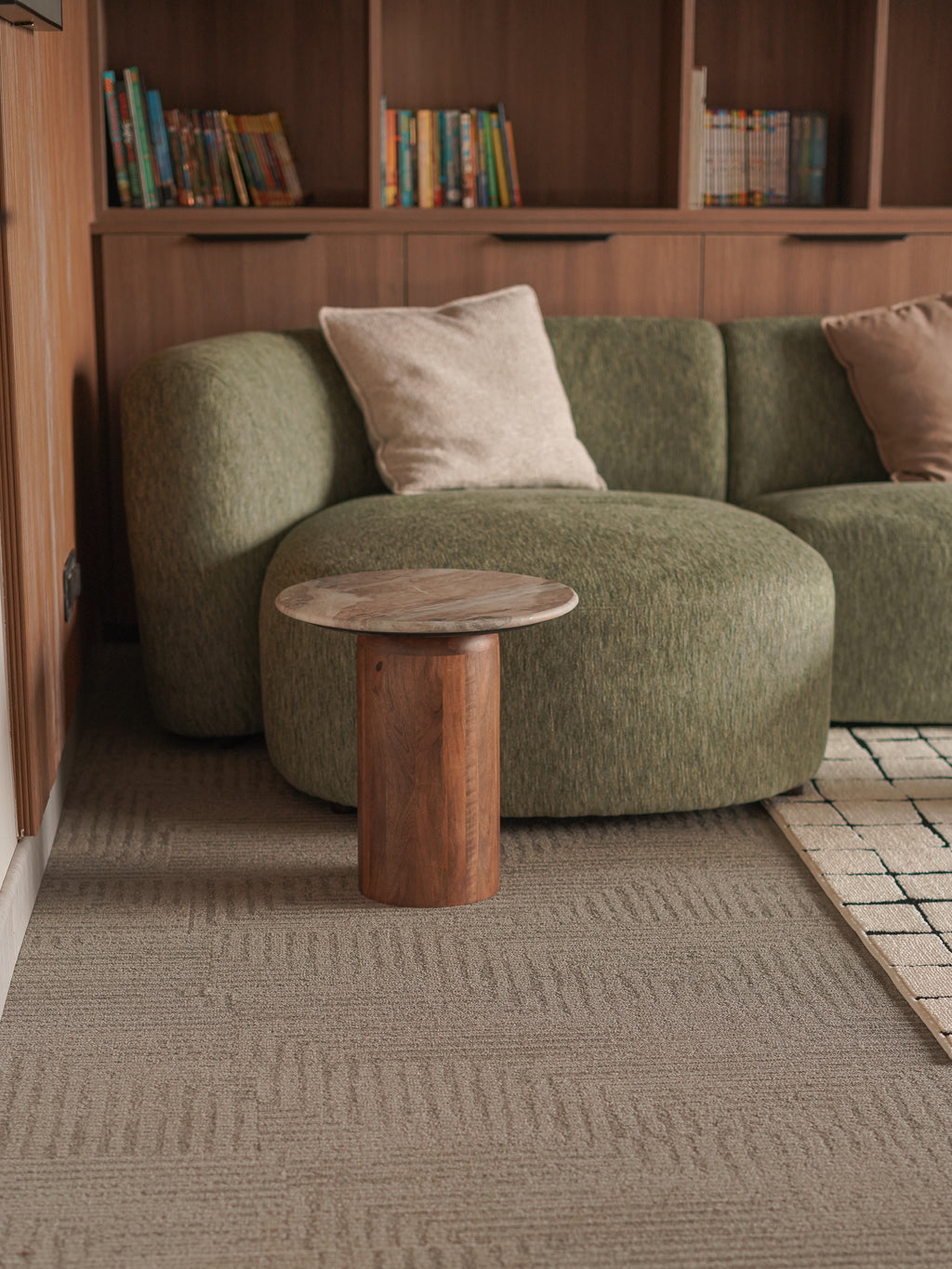 Green sofa with wooden side table and books on shelves in a room.