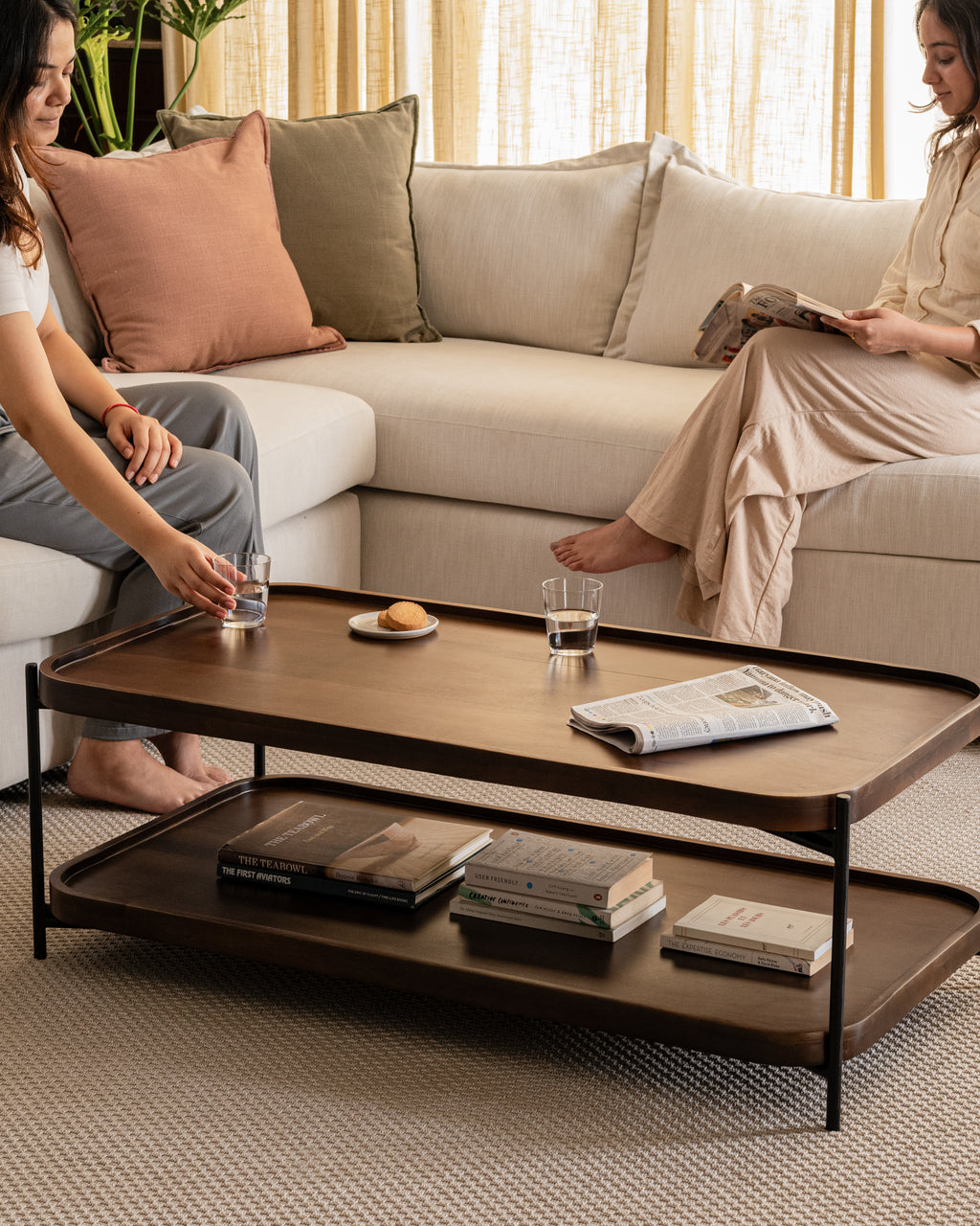 Elegant rectangular wood and metal coffee table with open shelf, styled in a modern neutral-toned living room.