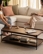 Elegant rectangular wood and metal coffee table with open shelf, styled in a modern neutral-toned living room.