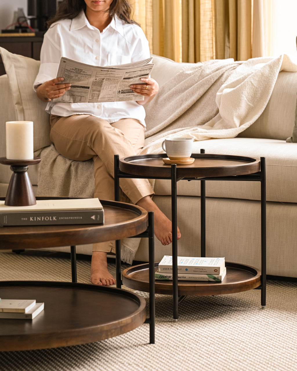 Cozy living space with nested coffee tables, side table, and woman relaxing with newspaper.