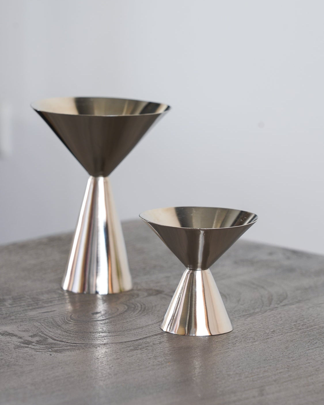 Steelcone-shaped cocktail glasses, one larger and one smaller, displayed on a gray wooden surface against a light gray background.